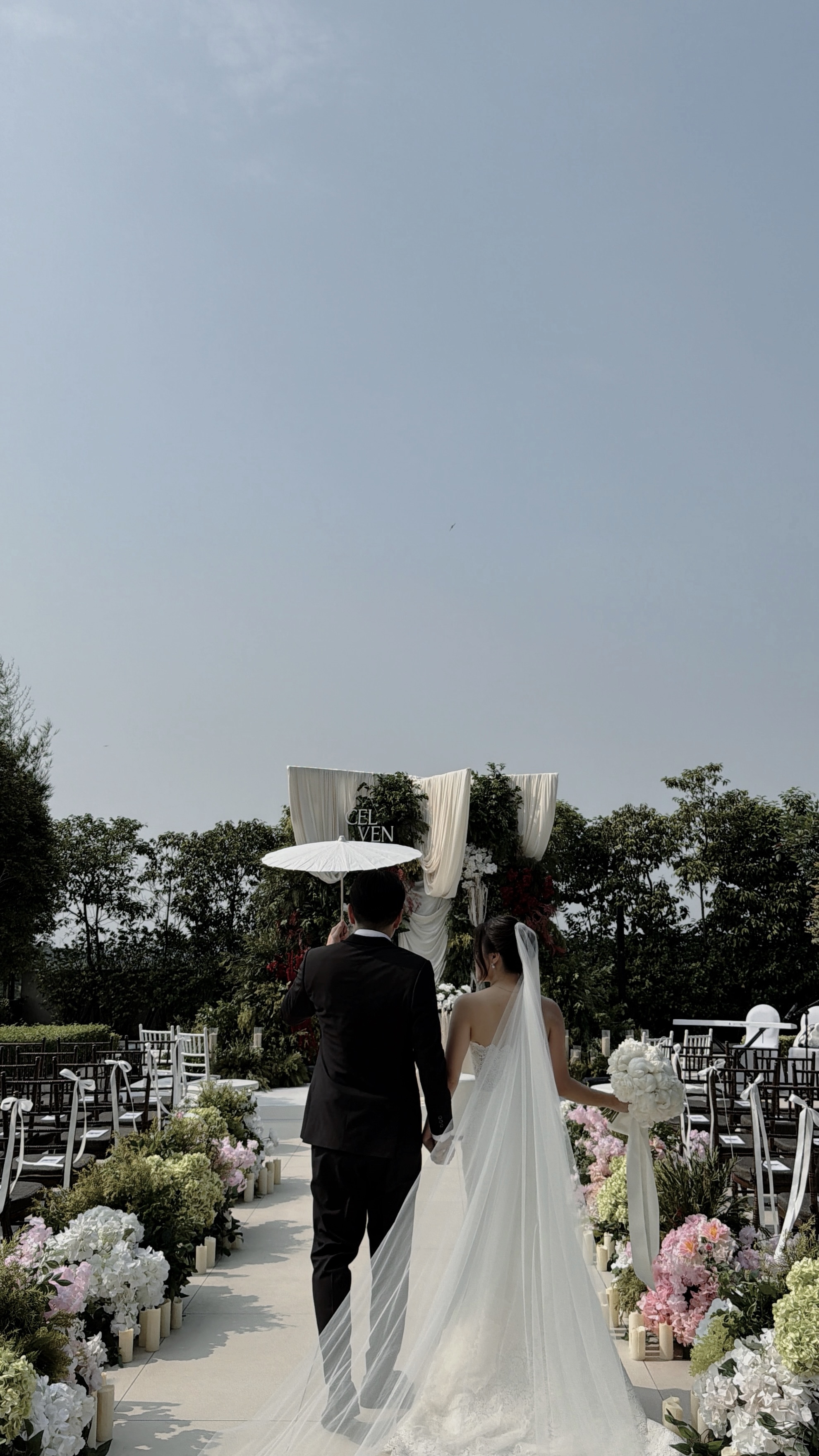 Couple walking the garden aisle under a parasol