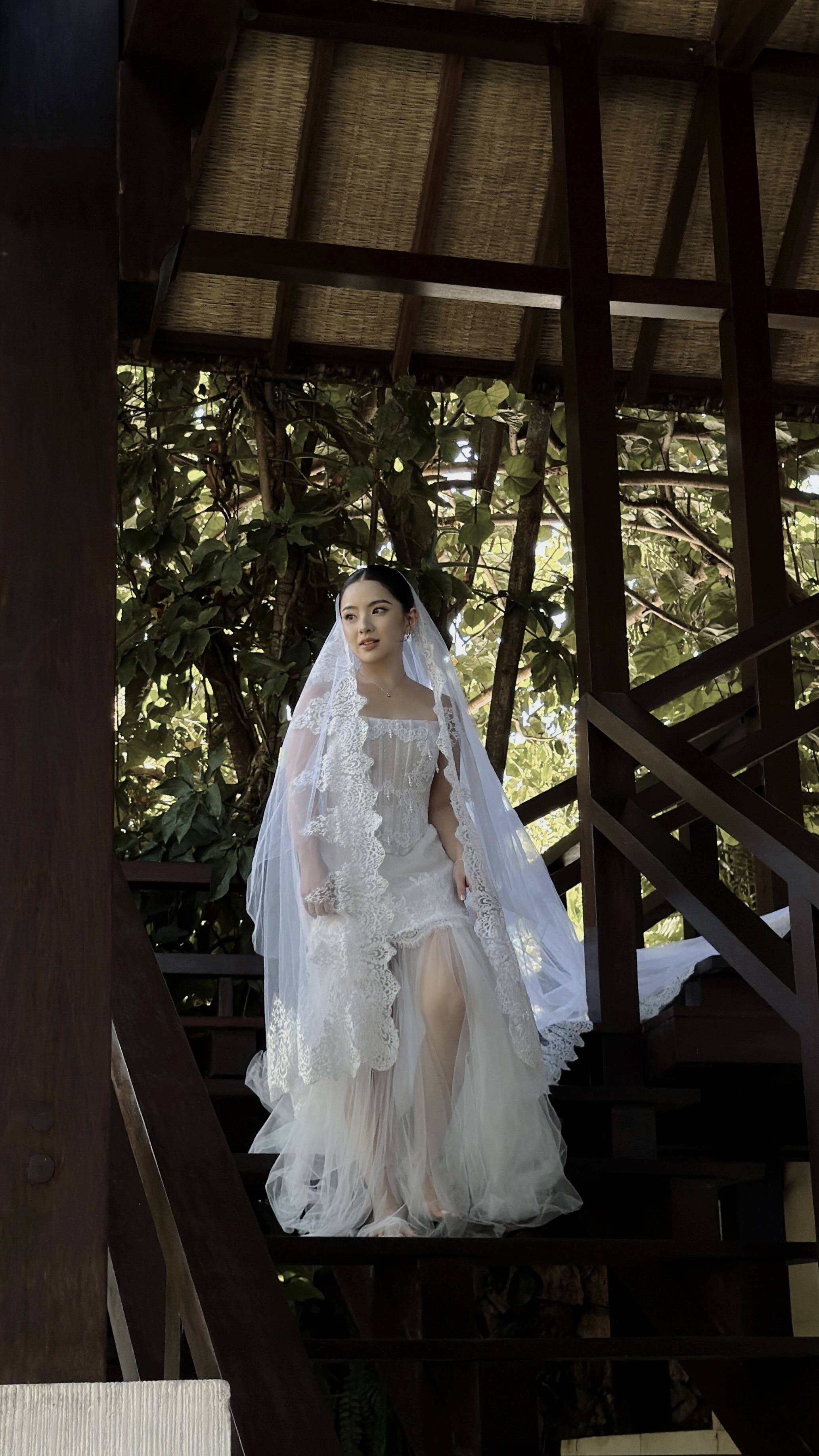 Bride on wooden villa stairs amid greenery